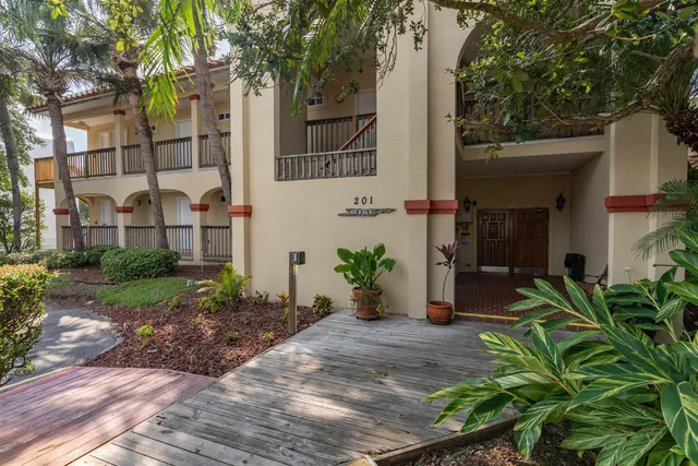 a view of a house with brick walls plants and large tree