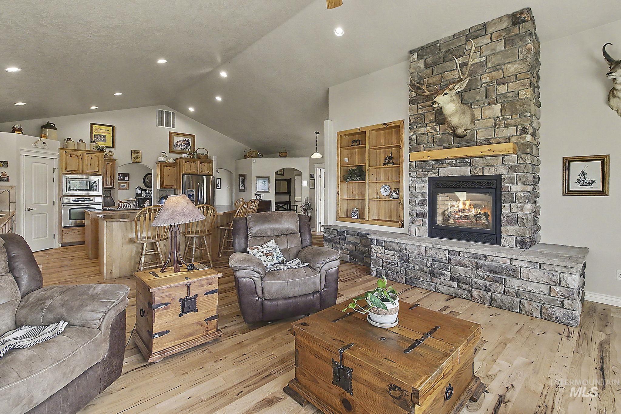6900 West Charters Lane Melba, ID 83641 - Photo 11 of 49 Stone-clad fireplace with hearth, vaulted ceilings, recessed lighting, wood-finish flooring, and built-in shelving