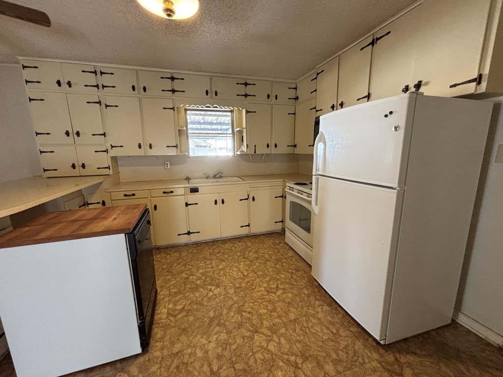 306 South Broadway Street Rocksprings, TX 78880 - Photo 10 of 23 a kitchen with granite countertop a refrigerator a sink and white cabinets