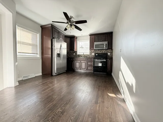 a living room with stainless steel appliances wooden floors and kitchen view