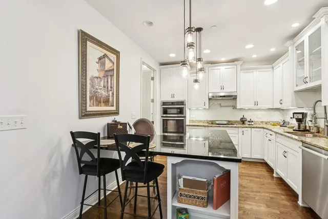 a kitchen with stainless steel appliances granite countertop a stove top oven a sink a refrigerator and white cabinets with wooden floor