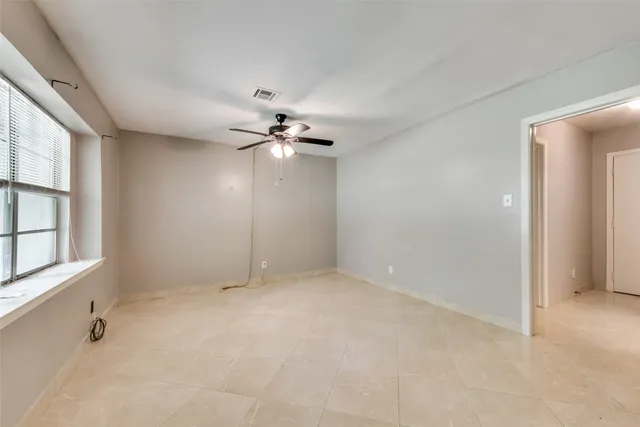 an empty room with chandelier fan and windows