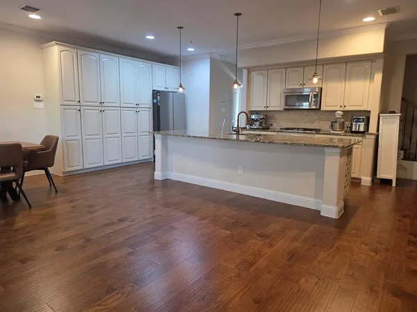 a kitchen with stainless steel appliances granite countertop a refrigerator a stove a sink a microwave and white cabinets with wooden floor