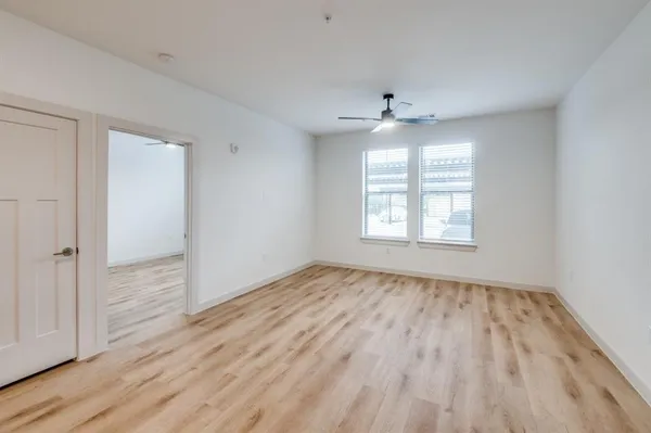 an empty room with wooden floor chandelier fan and windows