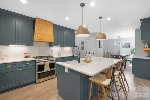 a kitchen with stainless steel appliances granite countertop a stove a sink a oven a dining table and chairs with wooden floor
