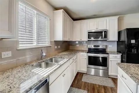 a kitchen with granite countertop a sink a counter top space appliances and cabinets