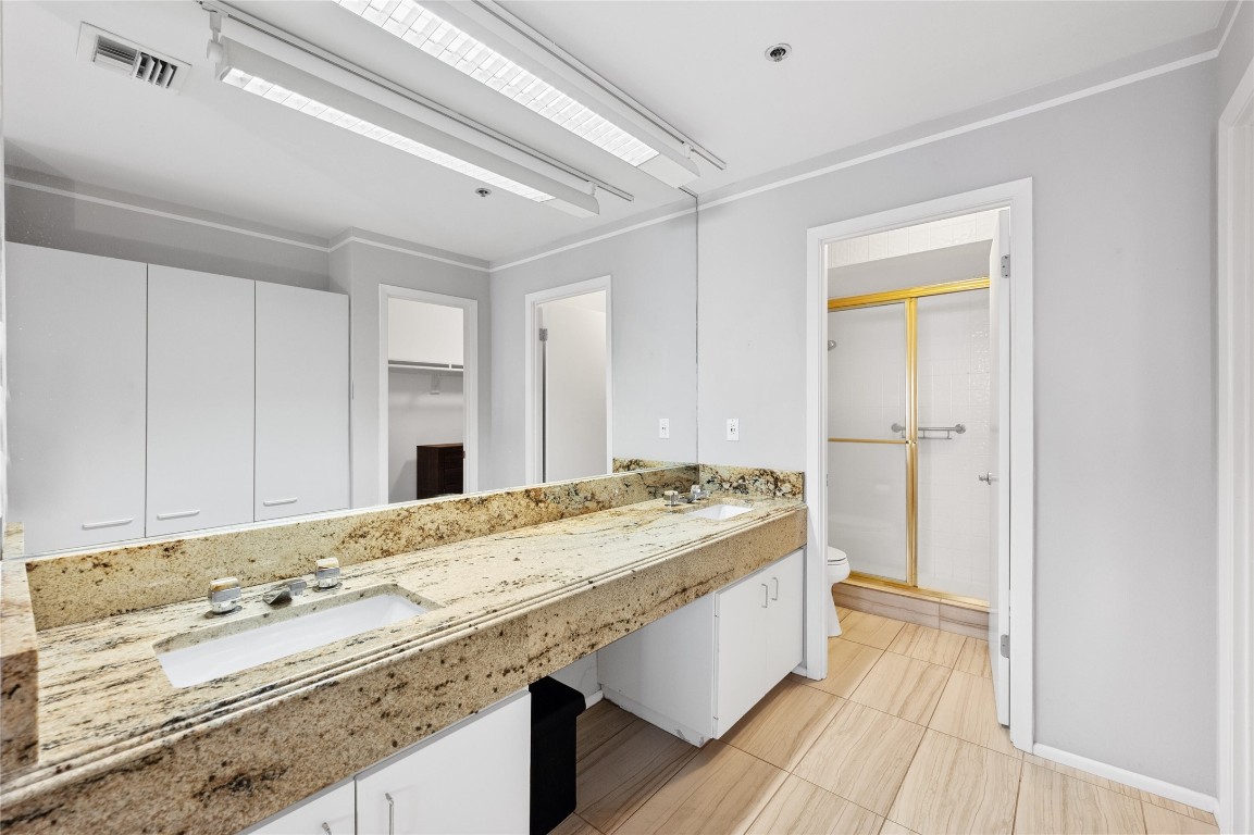 40 North Interstate Highway 35, Unit 2B2 Austin, TX 78701 - Photo 6 of 14 The master bathroom is designed for both style and convenience. It features a dual vanity set-up, accompanied by a generously sized mirror adorned with lights for optimal visibility. Ample storage solutions ensure a clutter-free environment. A walk-in shower offers a modern bathing experience.