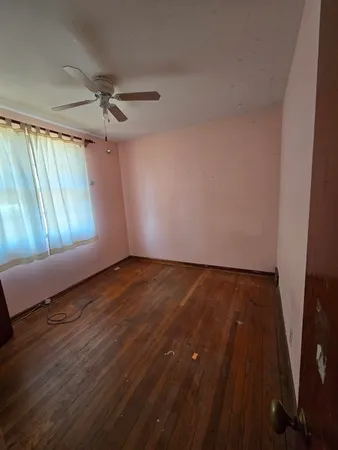 an empty room with wooden floor fan and windows