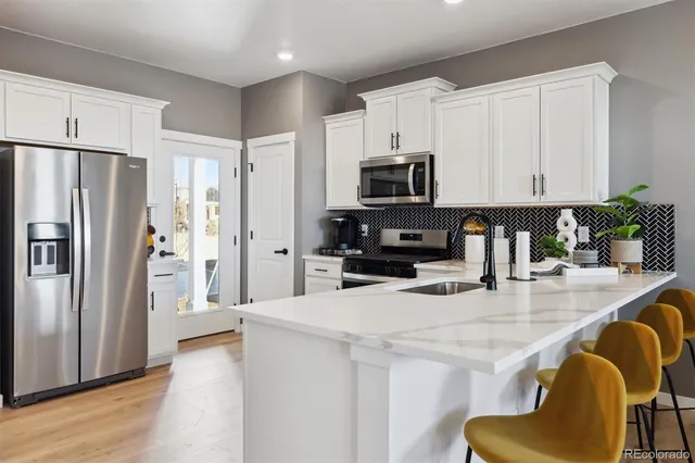 a kitchen with stainless steel appliances granite countertop a refrigerator a stove a sink a dining table and chairs with wooden floor