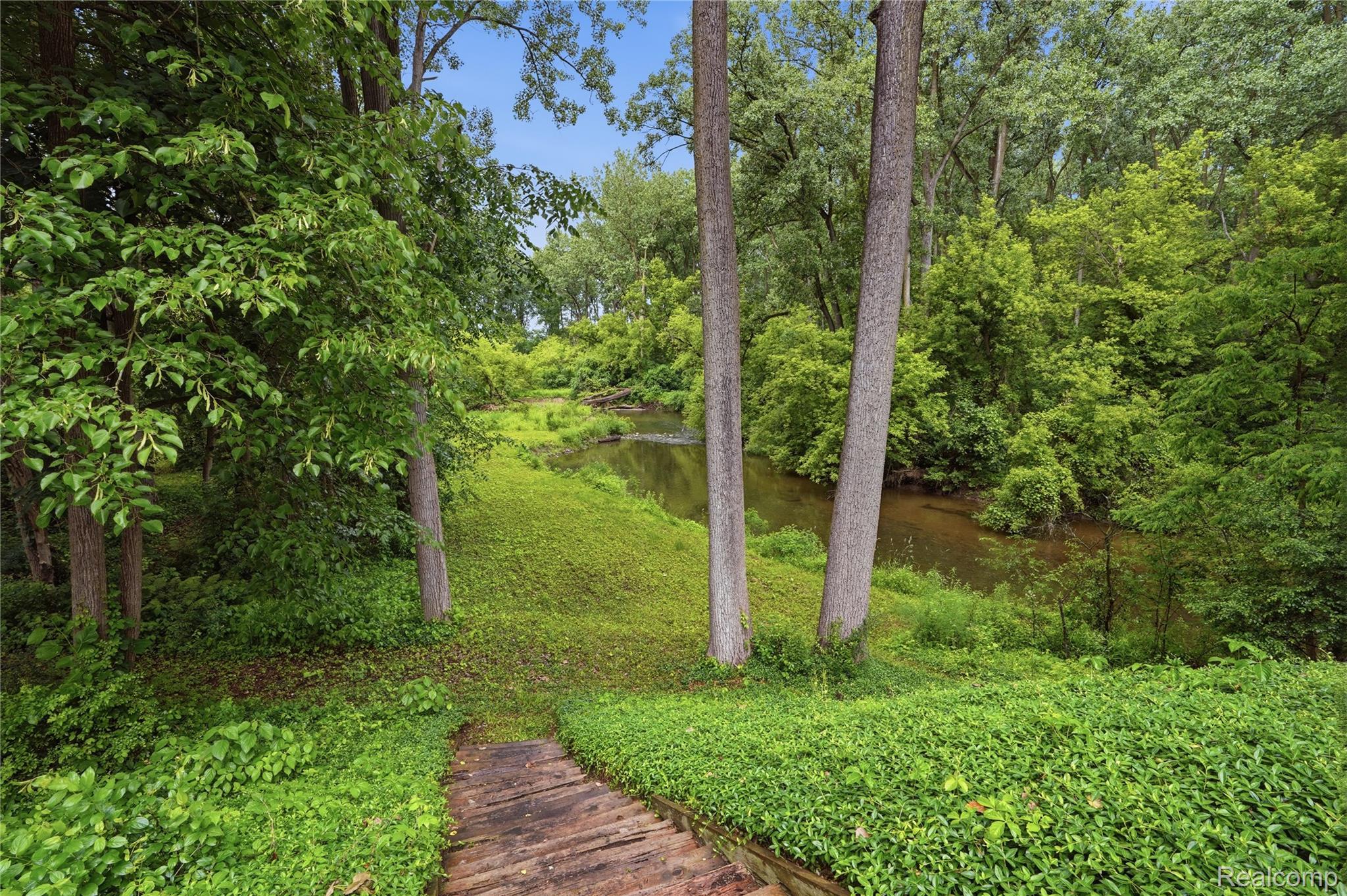 68345 Romeo Plank Road Ray, MI 48096 - Photo 12 of 52 Wood stairs leading to a verdant landscape with a natural water feature surrounded by mature trees and lush groundcover