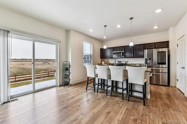 a living room with stainless steel appliances a dining table wooden floor and a large window