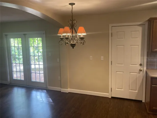 an empty room with wooden floor chandelier and windows