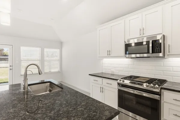 a kitchen with granite countertop a sink stove and microwave