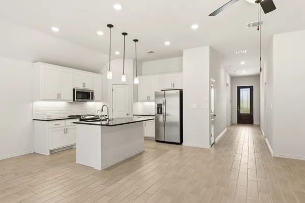 a kitchen with stainless steel appliances a refrigerator a sink dishwasher a stove and white cabinets with wooden floor
