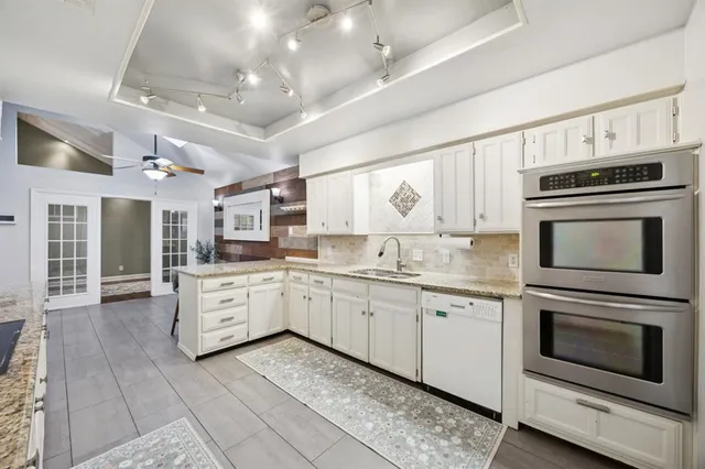 a kitchen with stainless steel appliances granite countertop a sink dishwasher and white cabinets with wooden floor