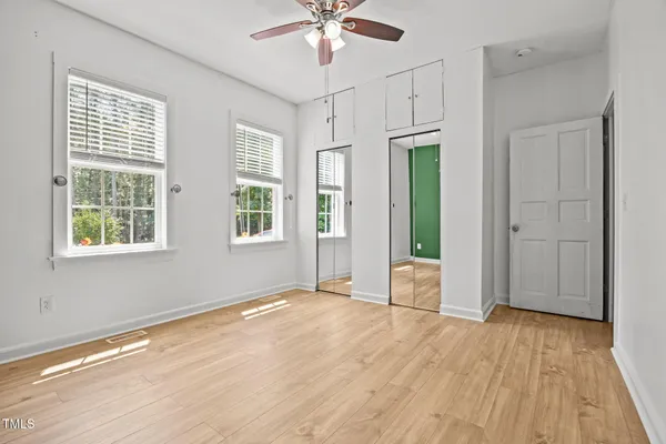 an empty room with wooden floor chandelier fan and windows