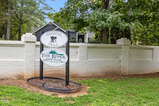 a sign board with a house and trees in the background