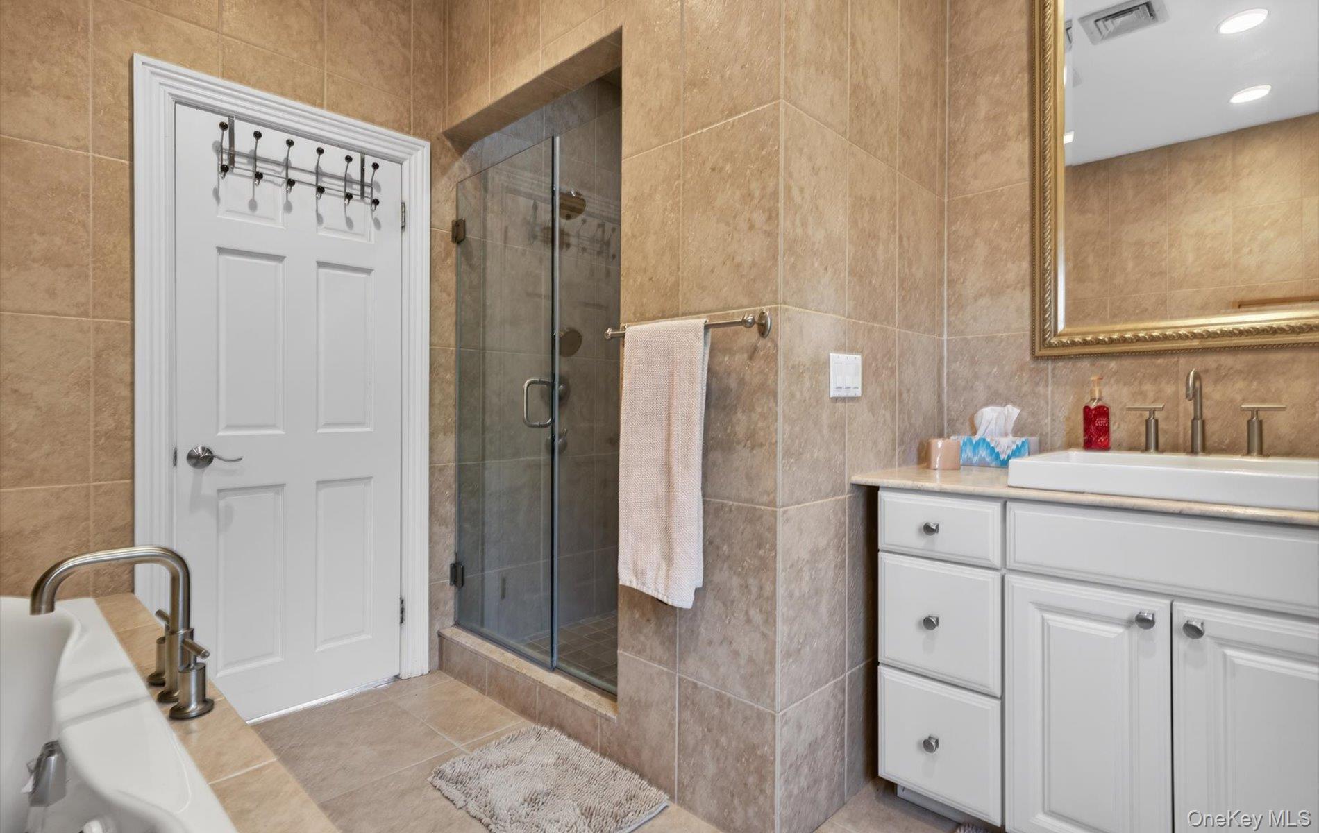 16 East Slope Road Bayville, NY 11709 - Photo 31 of 48 Bathroom featuring floor-to-ceiling natural stone tile, a glass-enclosed shower, and a white vanity with an undermount sink
