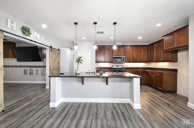 a kitchen with stainless steel appliances a stove top oven a sink dishwasher a refrigerator and a dining table with wooden floor