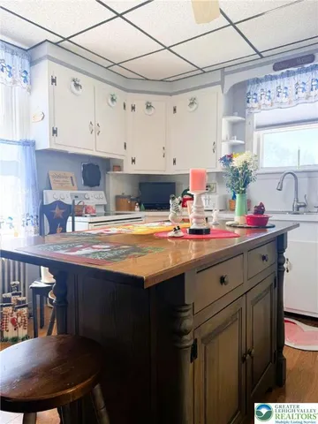 a room with kitchen island a sink a stove and white cabinets