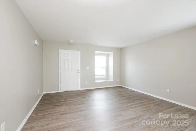 a view of an empty room with wooden floor and window