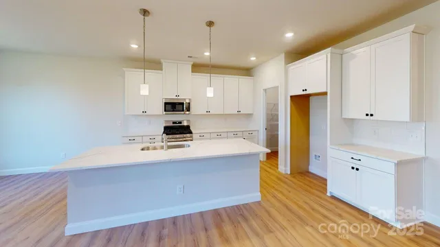 a large kitchen with stainless steel appliances a large counter top a stove a refrigerator white cabinets and wooden floor