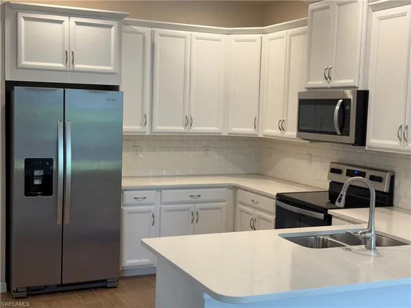 a kitchen with stainless steel appliances granite countertop a refrigerator a sink a stove and white cabinets