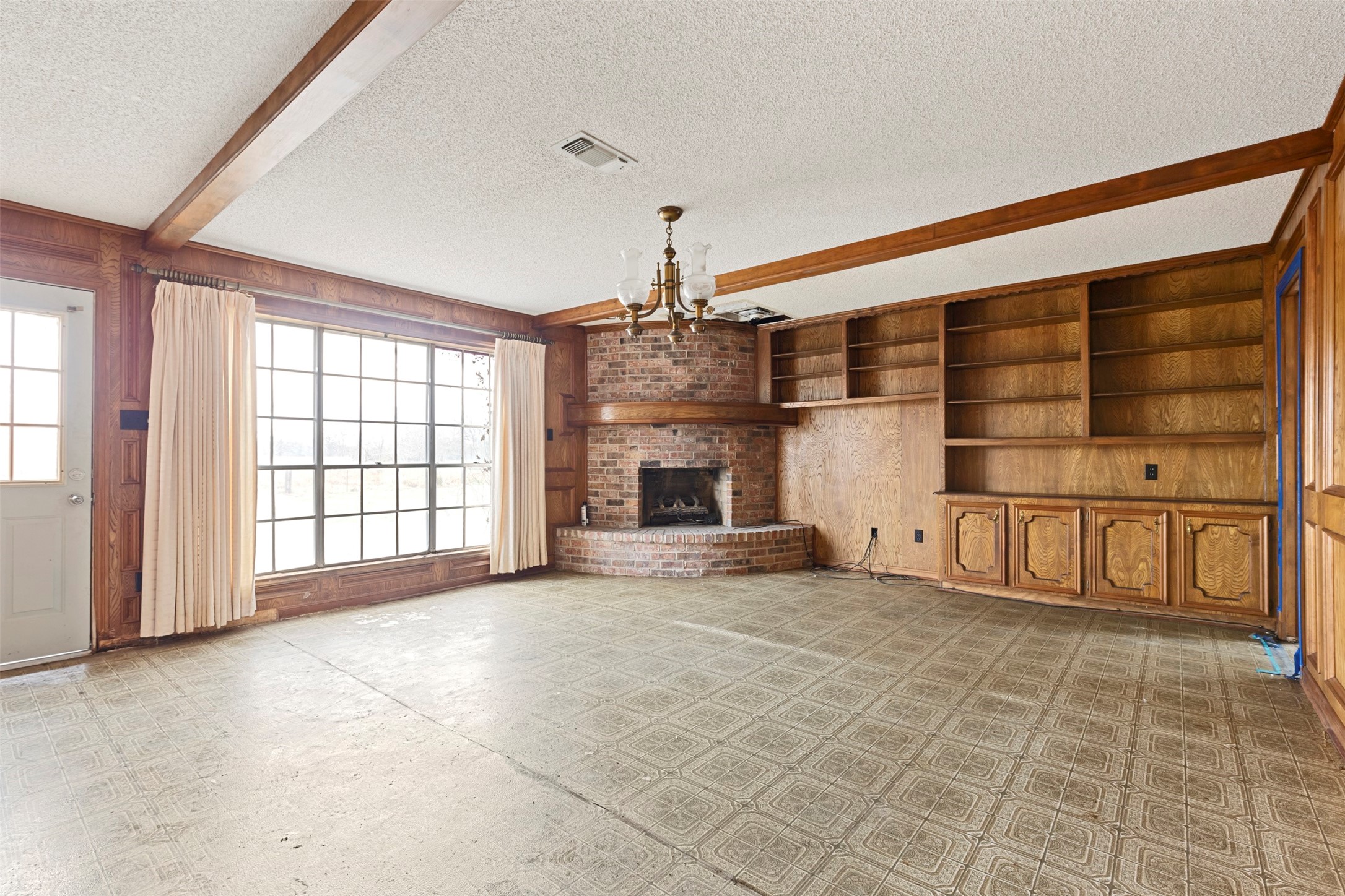 22279 Chapman Road Hempstead, TX 77445 - Photo 23 of 28 Living room with wooden beams on the ceiling. Bookshelves and cabinets built into the walls. A curved brick fireplace and wooden mantle.