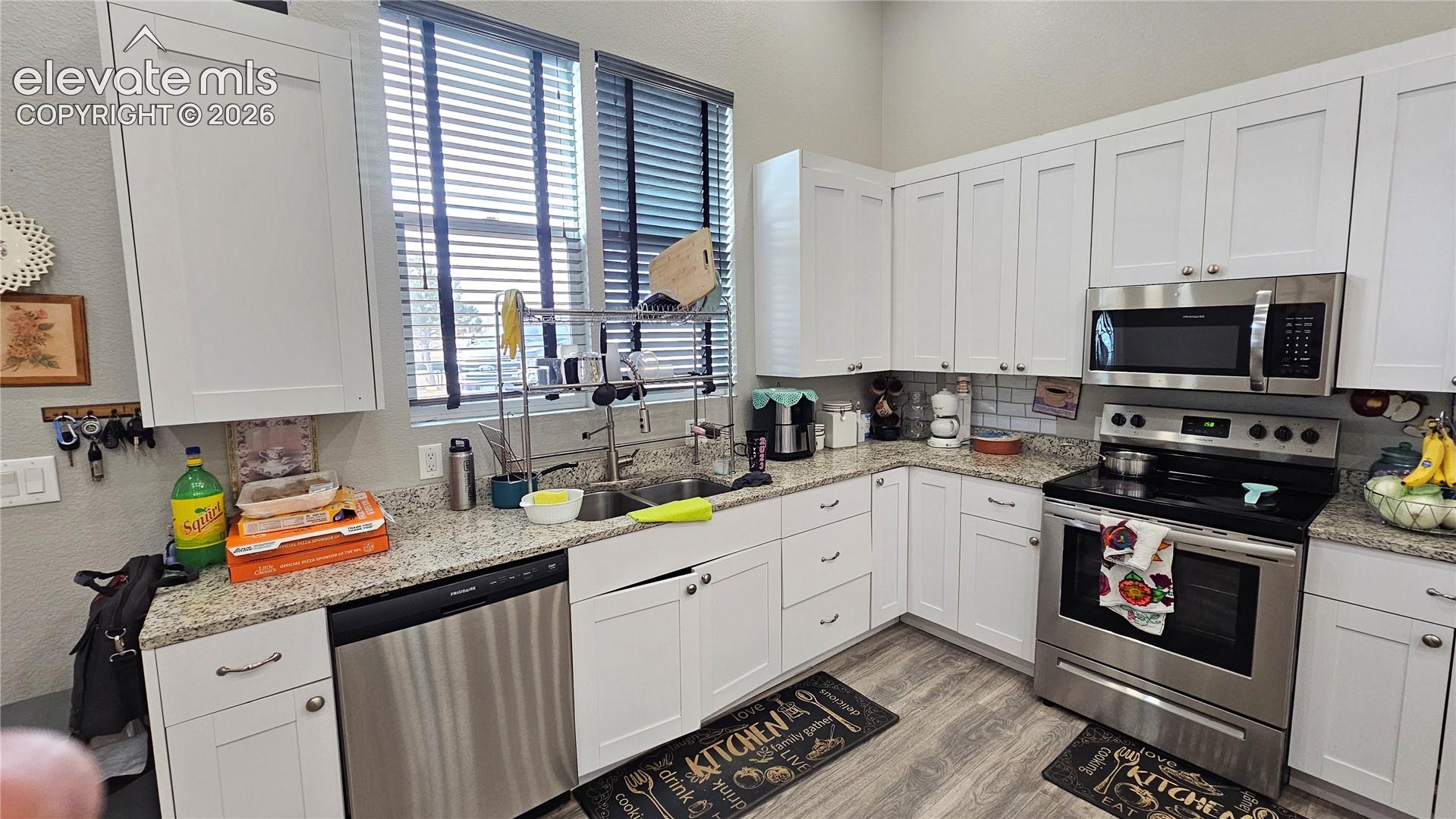 3835 Sengbeil Road Yoder, CO 80864 - Photo 14 of 48 Kitchen featuring white shaker cabinetry, stainless steel appliances, speckled stone countertops, and wood-finish flooring