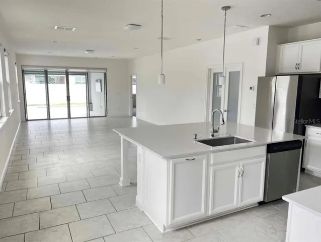 a kitchen with stainless steel appliances kitchen island granite countertop a refrigerator a sink and white cabinets