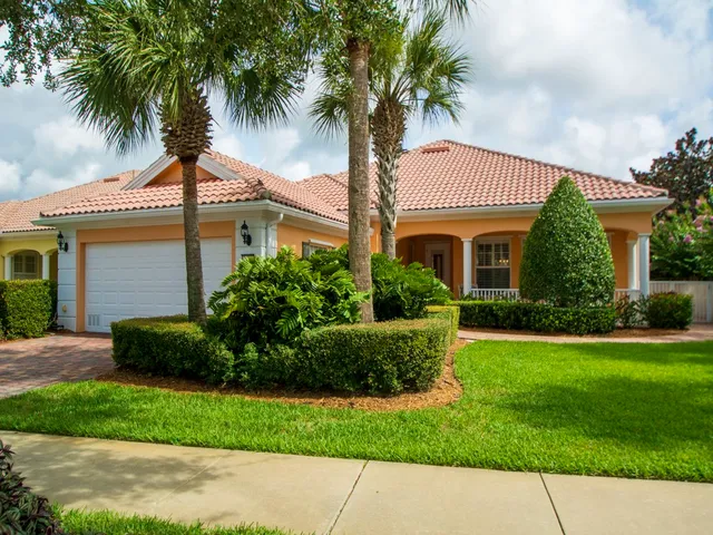 a front view of a house with a garden and palm trees