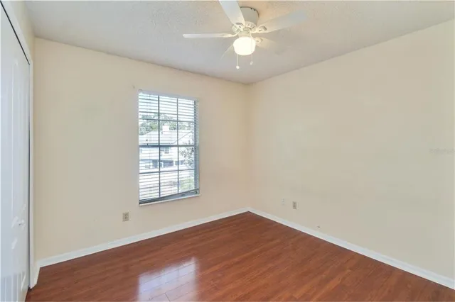 an empty room with wooden floor fan and windows
