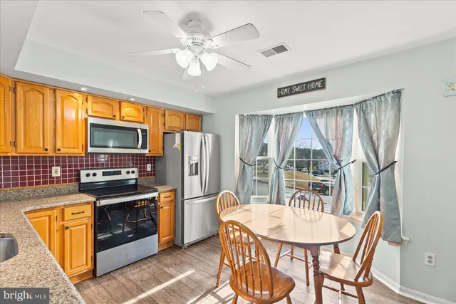 a kitchen with stainless steel appliances granite countertop a stove a refrigerator a sink dishwasher a dining table and chairs with wooden floor
