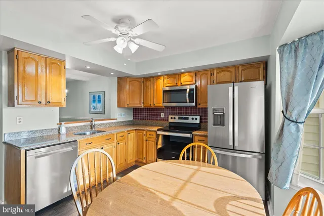 a kitchen with stainless steel appliances granite countertop a refrigerator a sink dishwasher a stove a dining table and chairs with wooden floor