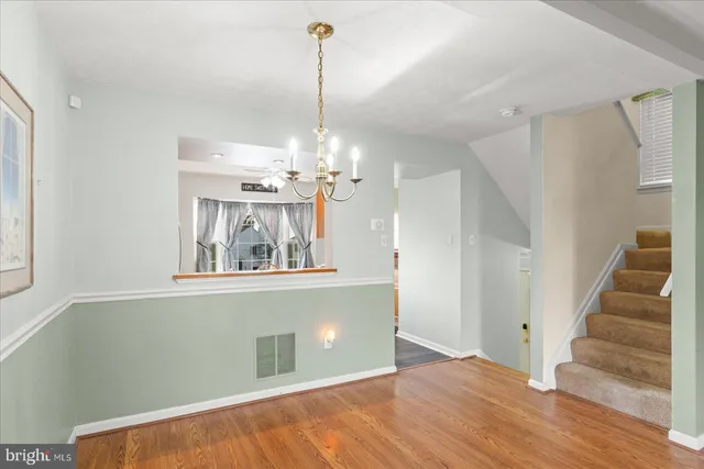 a view of an empty room with wooden floor kitchen view and a window