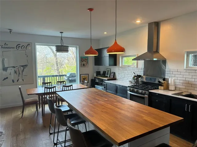 a kitchen with stainless steel appliances granite countertop a stove a refrigerator a kitchen island a dining table and chairs with wooden floor