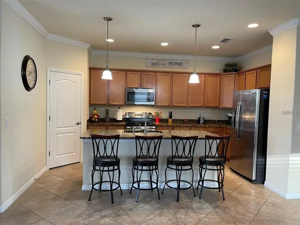 a kitchen with kitchen island granite countertop a dining table chairs refrigerator and cabinets