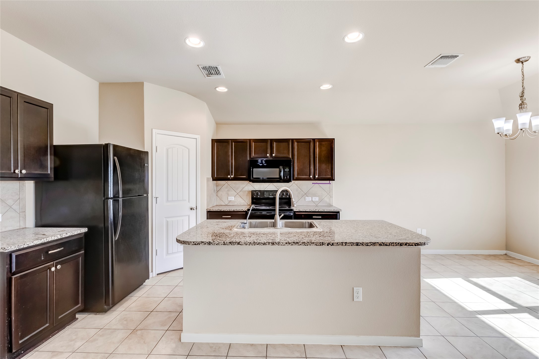 100 Sulphur River Loop Hutto, TX 78634 - Photo 8 of 16 Kitchen featuring dark brown cabinetry, a center island with sink, black appliances, decorative backsplash, and light stone counters