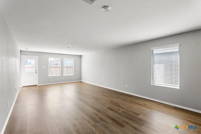 a view of an empty room with wooden floor and window