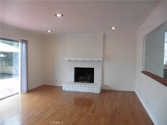 a view of an empty room with wooden floor fireplace and a window