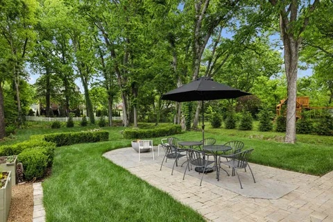 a view of a table and chairs in backyard under a large tree