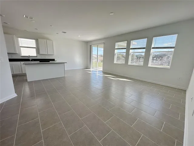 a view of an empty room with kitchen and window