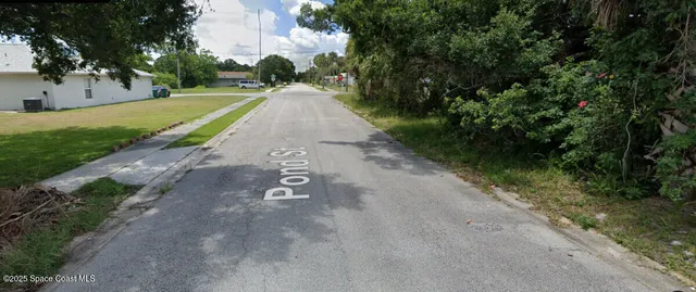 a view of a street with a yard and a large trees
