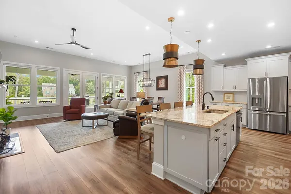 a kitchen with stainless steel appliances granite countertop a refrigerator a sink dishwasher a oven and a dining table with wooden floor