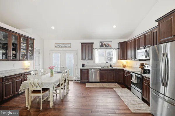 a kitchen with stainless steel appliances granite countertop a refrigerator a stove top oven a sink dishwasher and white cabinets with wooden floor