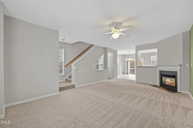 a view of an empty room with chandelier fan and fire place