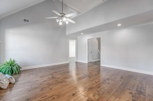a view of an empty room with wooden floor and a chandelier fan
