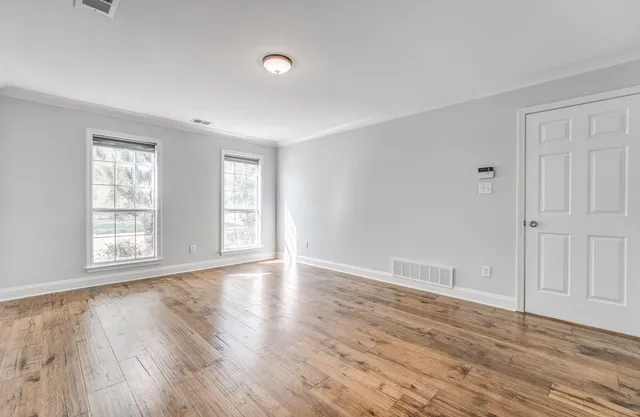 a view of an empty room with wooden floor and windows