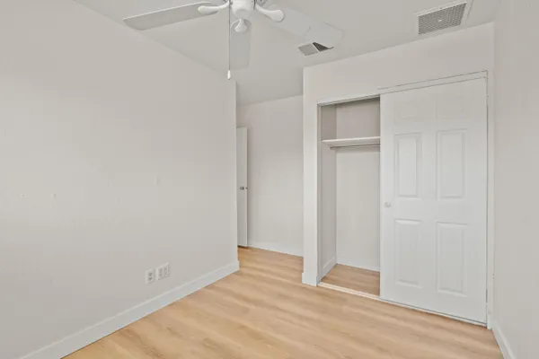 an empty room with wooden floor closet and windows