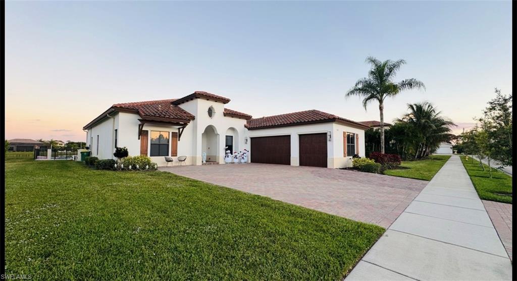 Mediterranean / spanish-style house featuring a yard, stucco siding, an attached garage, a tile roof, and decorative driveway